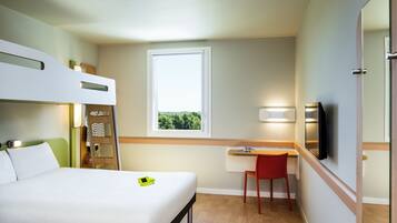 Une chambre d’hôtel avec un lit superposé, un bureau avec une chaise, une télévision et une fenêtre donnant sur un paysage verdoyant.
