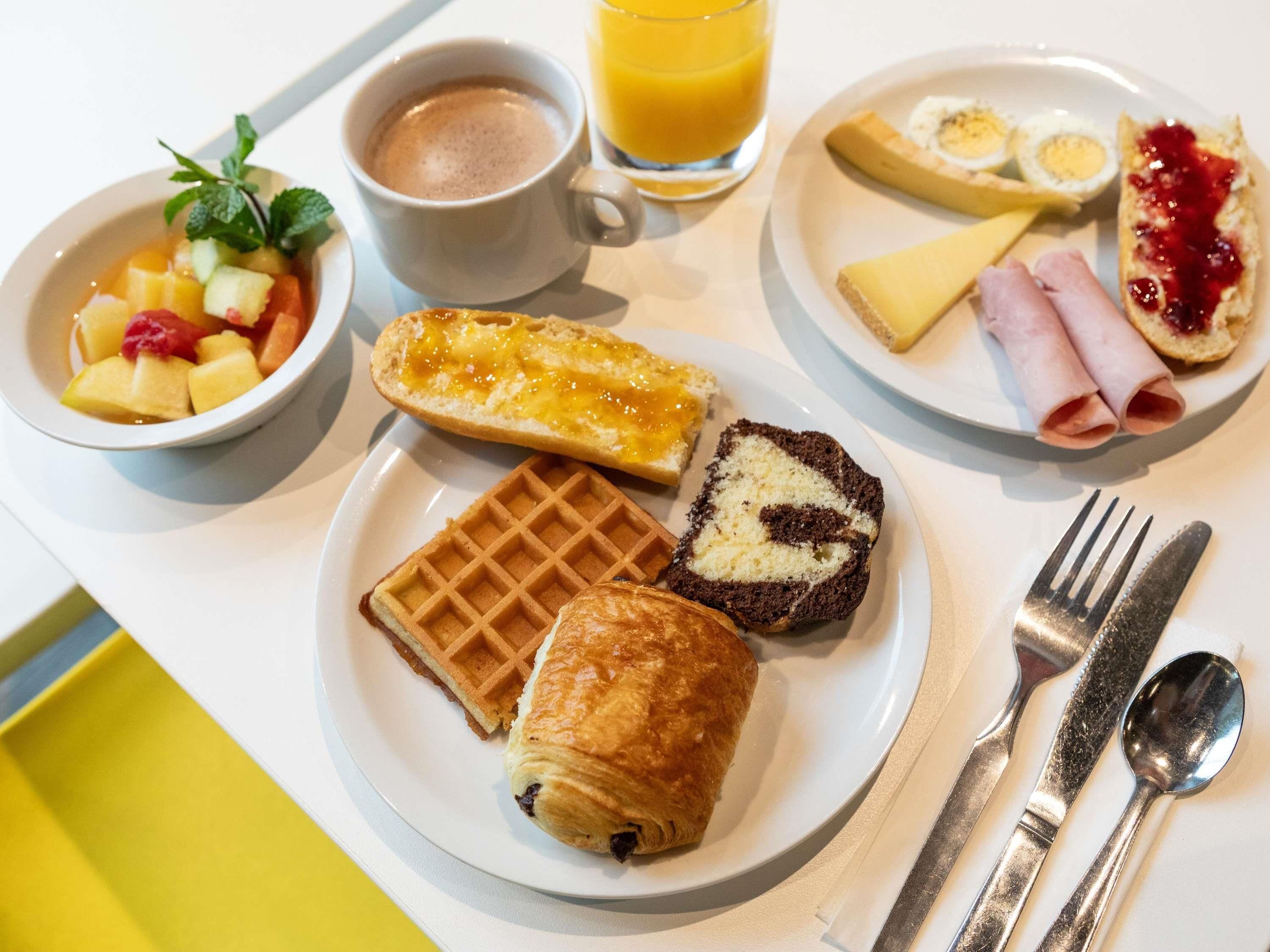 A breakfast setting with a waffle, croissant, and a plate with eggs, ham, and jam.