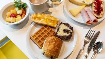 A breakfast setting with a waffle, croissant, and a plate with eggs, ham, and jam.