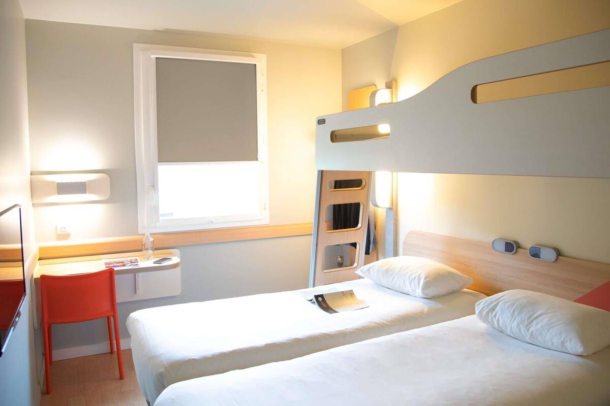 A compact hotel room with two beds, a desk, and a chair.