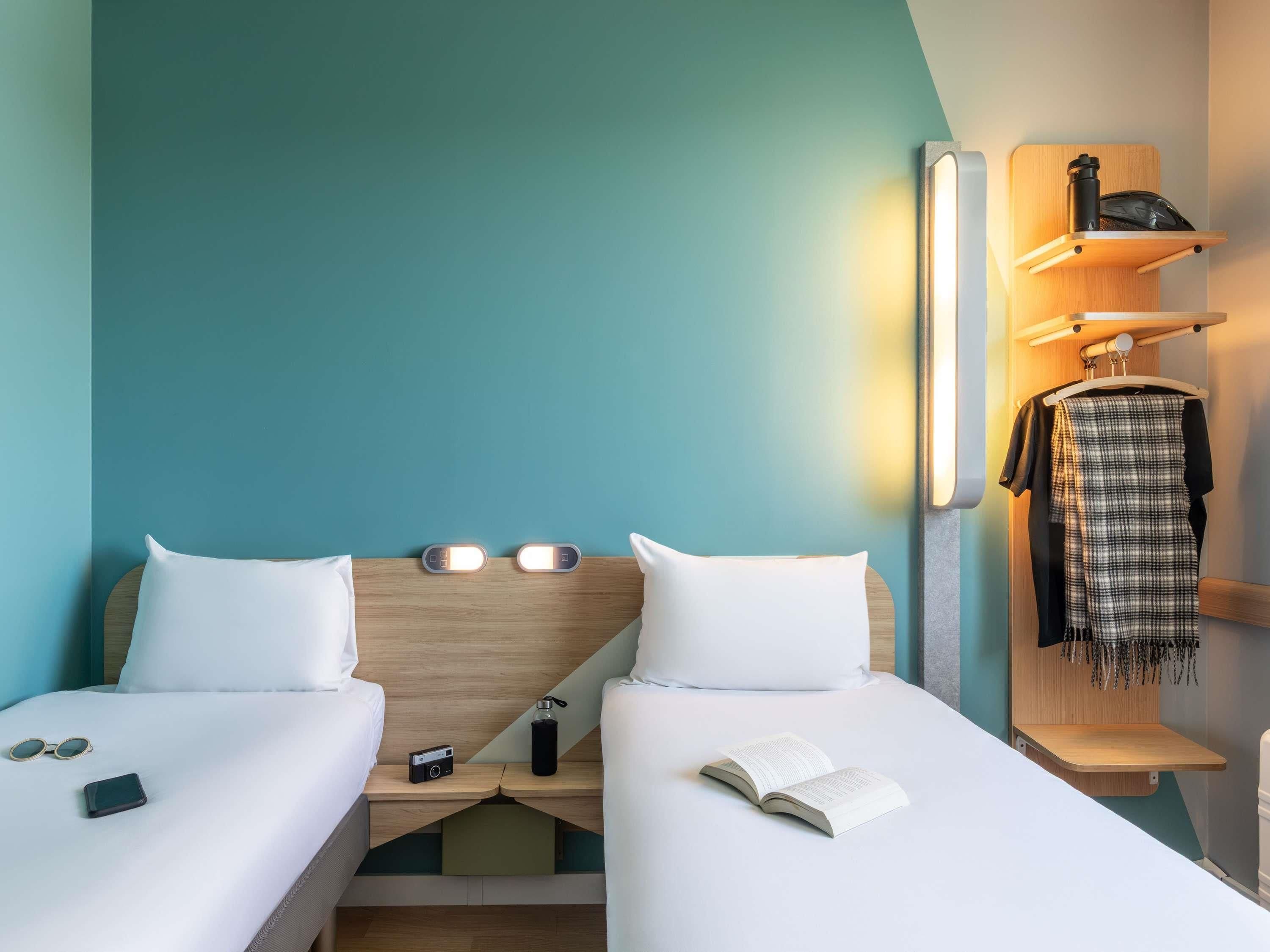 A hotel room with two beds, bedside tables, a wardrobe, and a mirror.