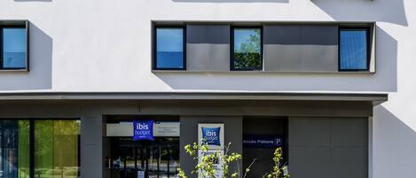 Un moderno edificio de hotel con un llamativo letrero de "ibis budget", amplias ventanas y una fachada limpia.