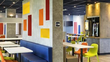 A modern dining area with colorful geometric wall art, a variety of seating options including benches and chairs, and a counter with a beverage dispenser.