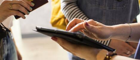 A person holding a passport and a tablet, with another individual reaching out to take it.