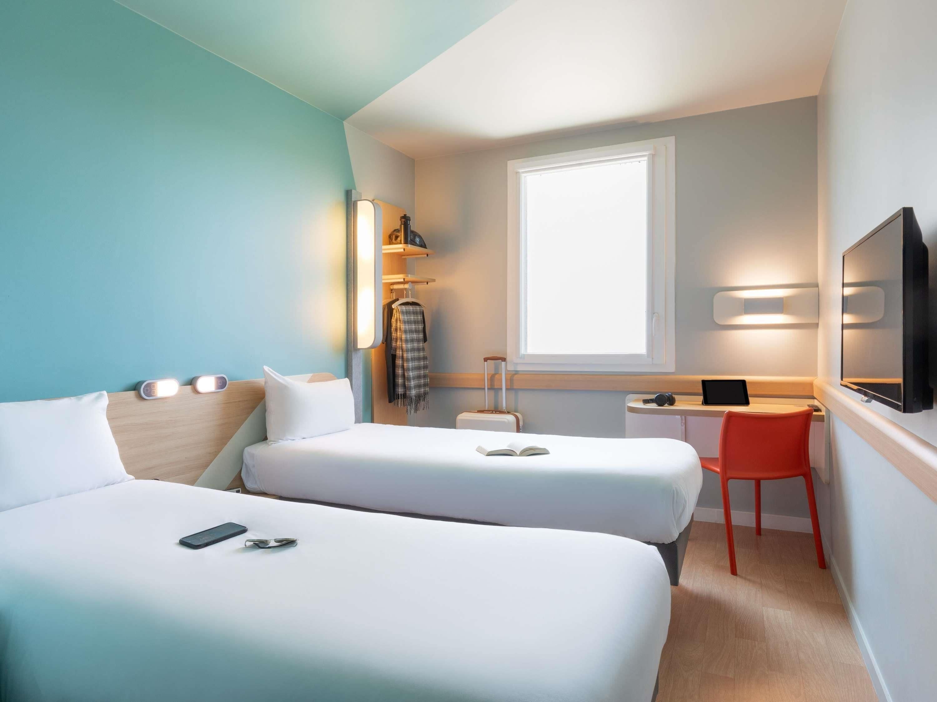 Habitación de hotel con dos camas, un escritorio, una silla, un televisor y una ventana.