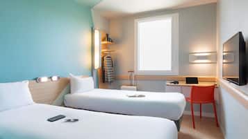 A hotel room with two beds, a desk, a chair, a TV, and a window.