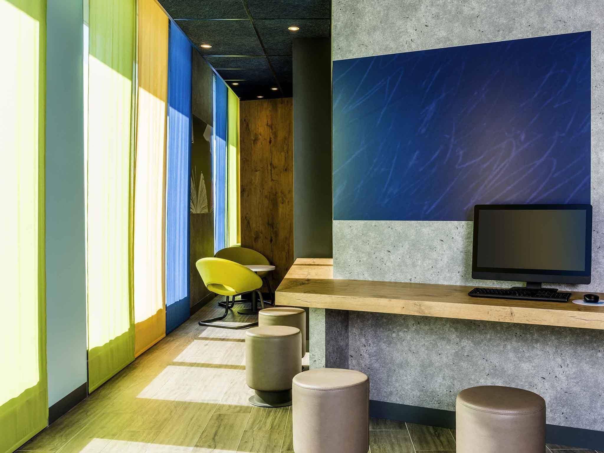 A modern office space with a long corridor, a wooden desk with a computer, and a yellow chair.