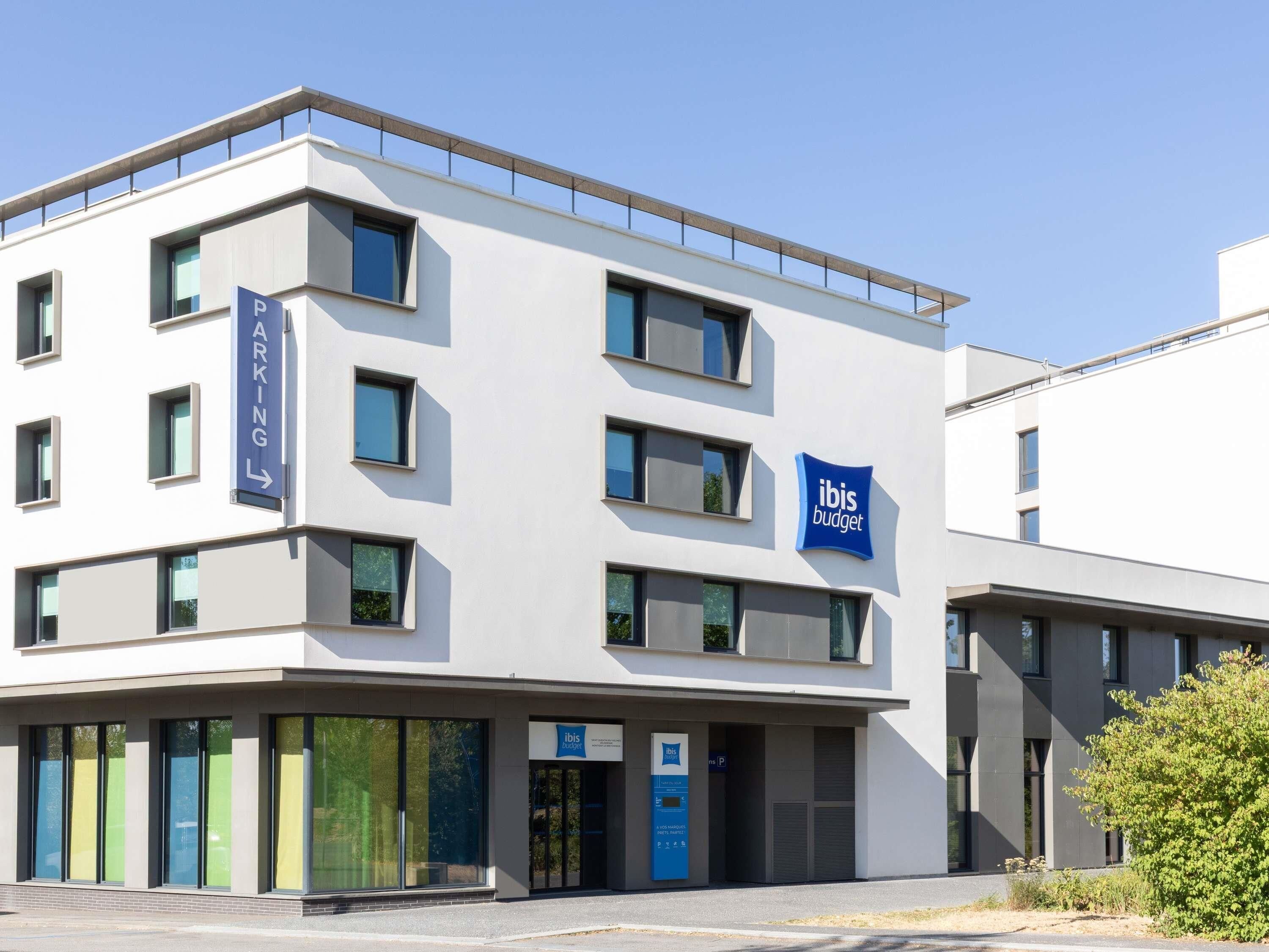 A modern building with a sign for ibis budget hotel, a parking sign, and a clear sky.