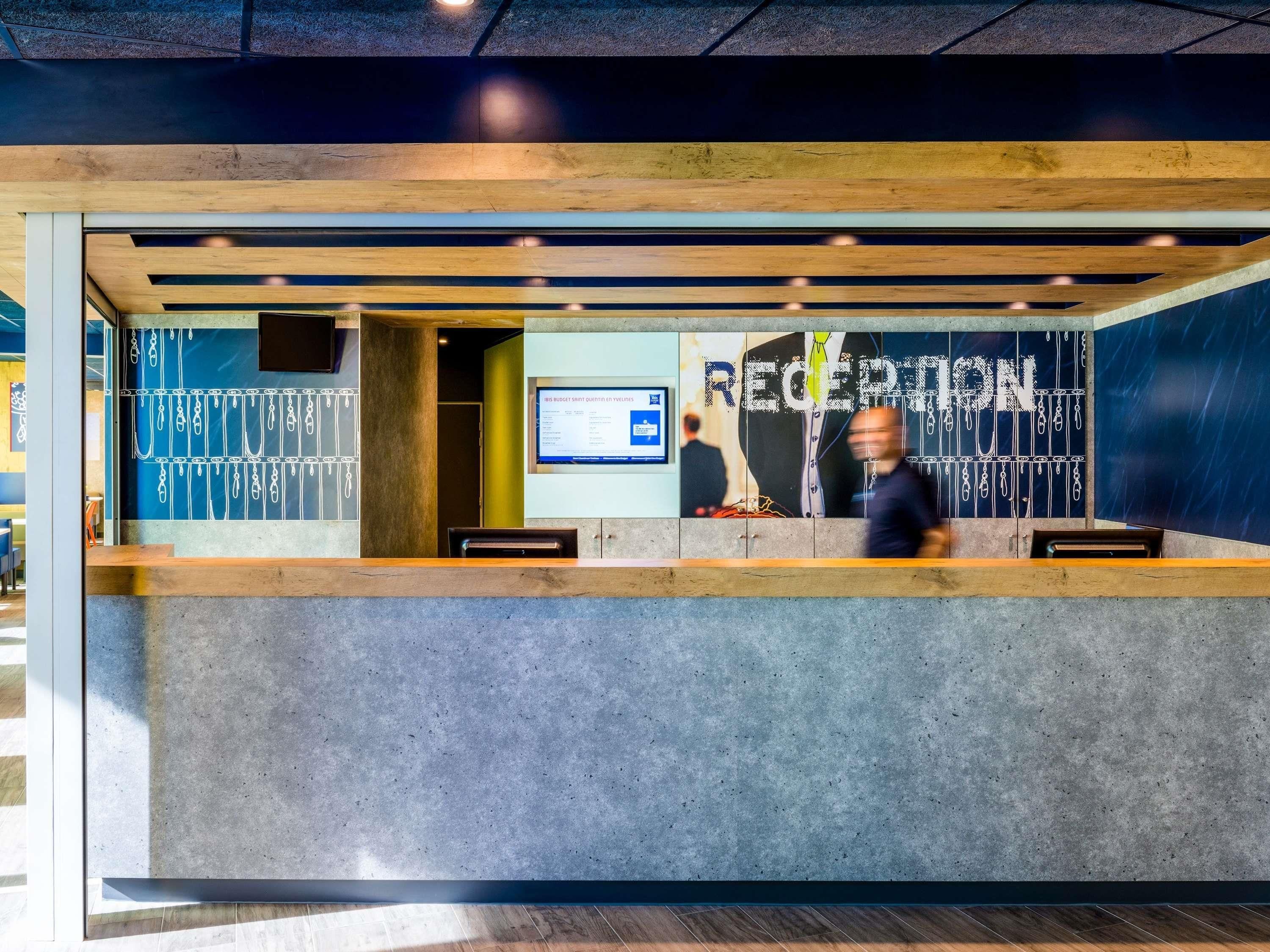 A reception desk with a digital screen, a wooden counter, and a wall with a graphic design.