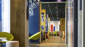 A modern interior with wooden flooring, colorful chairs, and a blue wall with white patterns. - ibis budget Saint Quentin en Yvelines Velodrome (Montigny-le-Bretonneux)