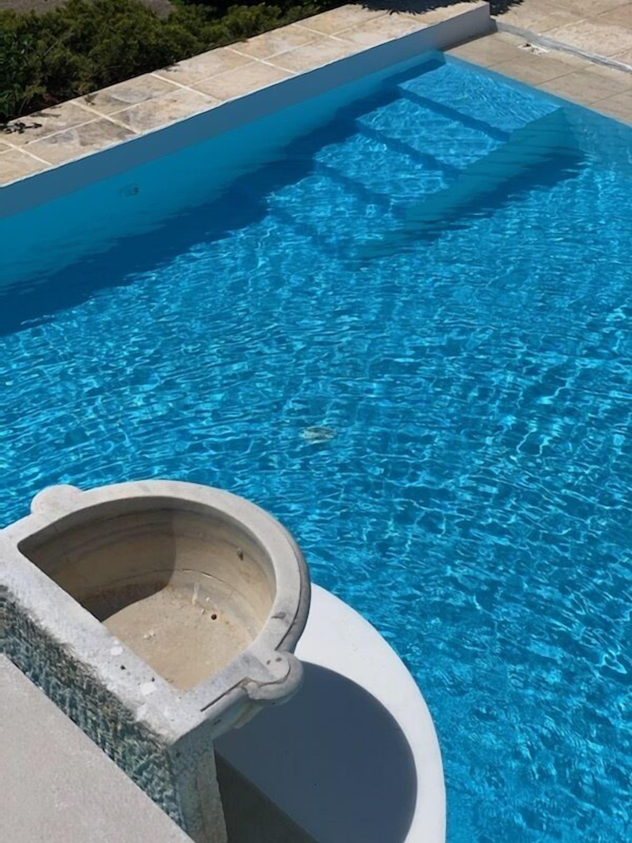 A swimming pool with clear blue water and a stone structure in the foreground.
