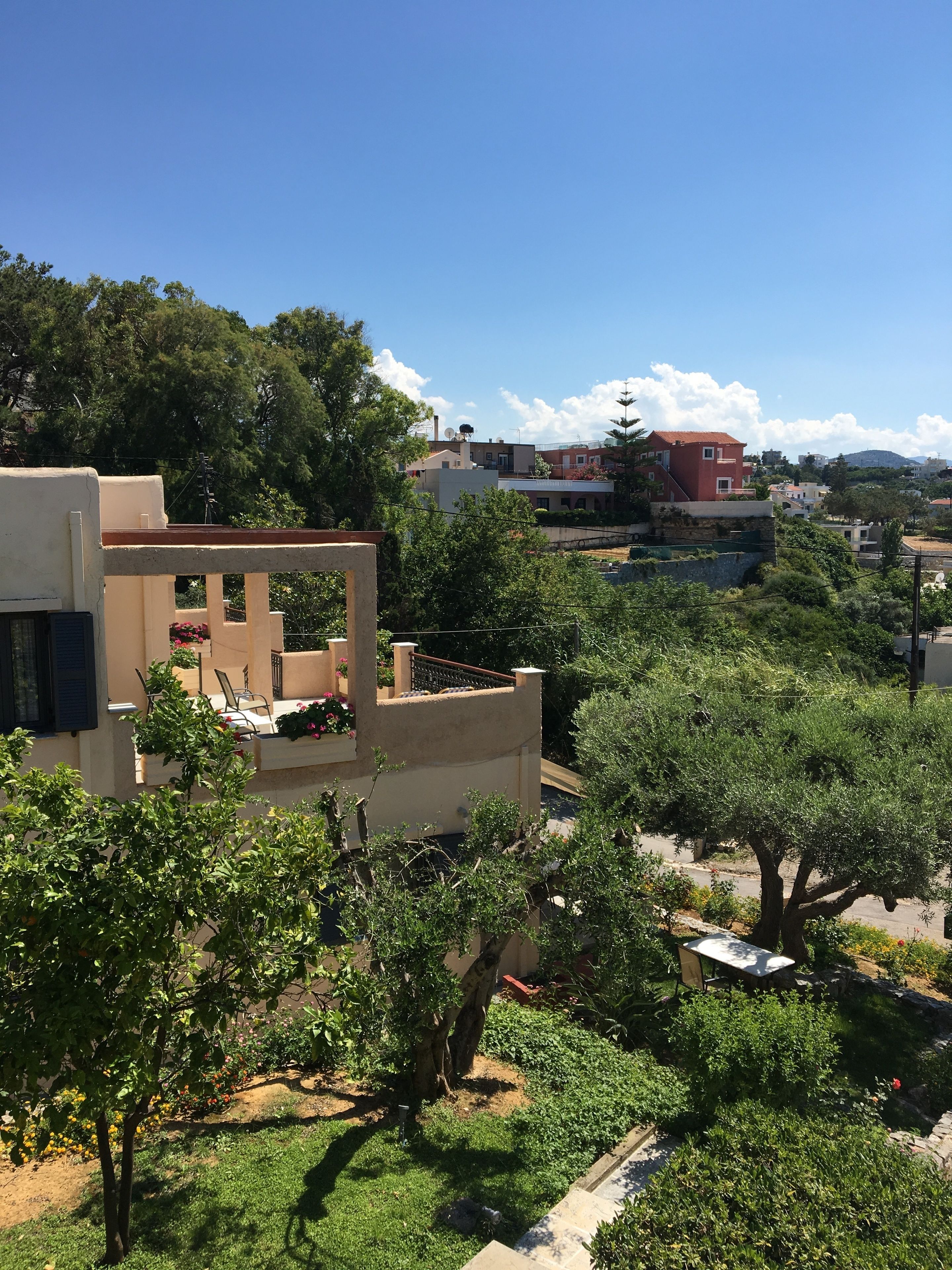 A residential area with a beige house featuring a balcony with outdoor furniture and potted plants.