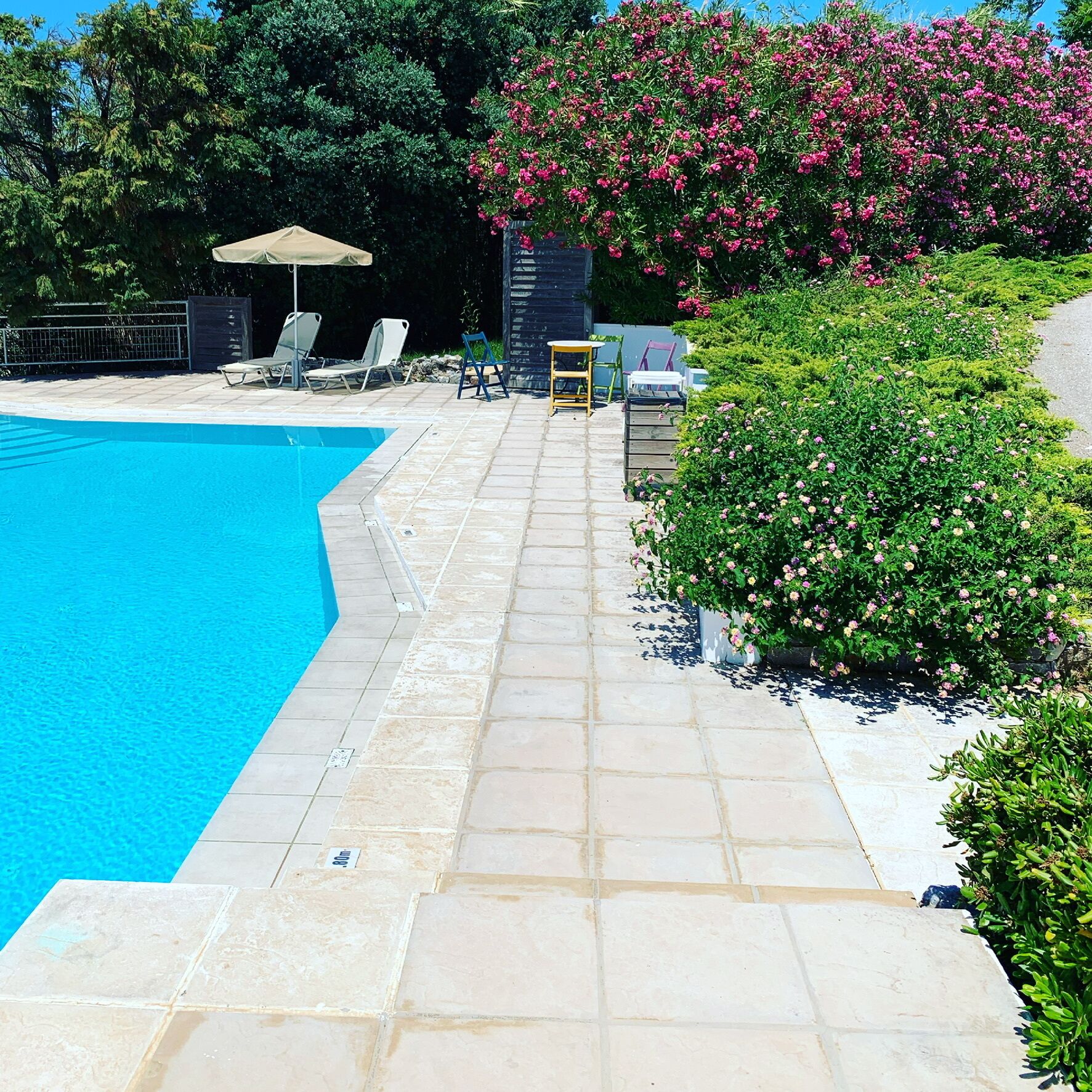 A swimming pool with a tiled deck, lounge chairs, and a small table.