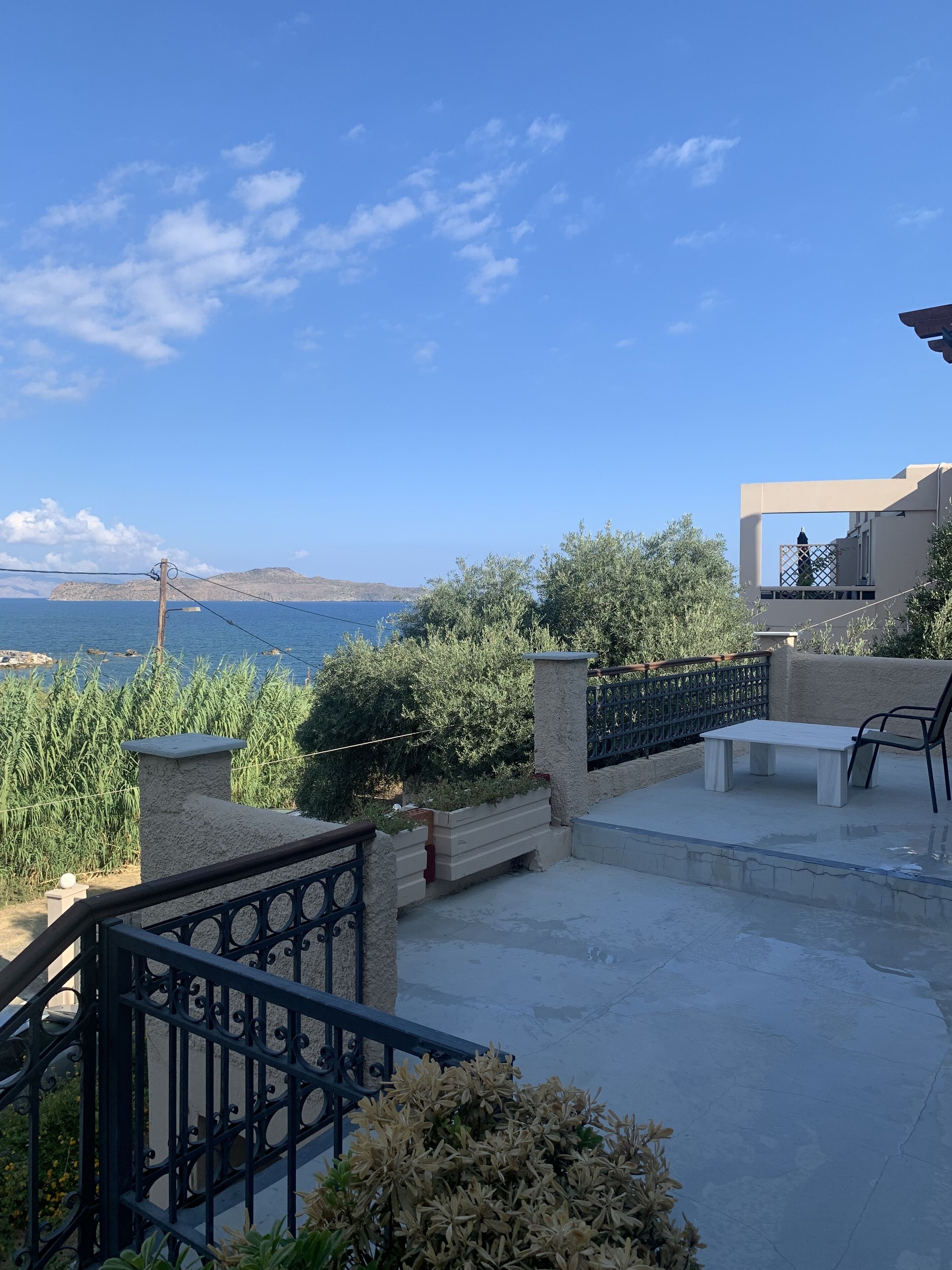 A terrace with a view of the sea, a stone bench, and a metal fence.