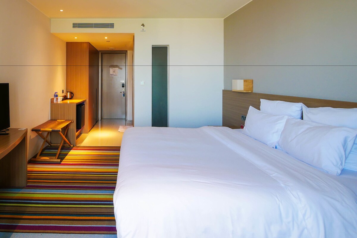 Habitación de hotel con cama, televisor, escritorio y alfombra colorida a rayas.