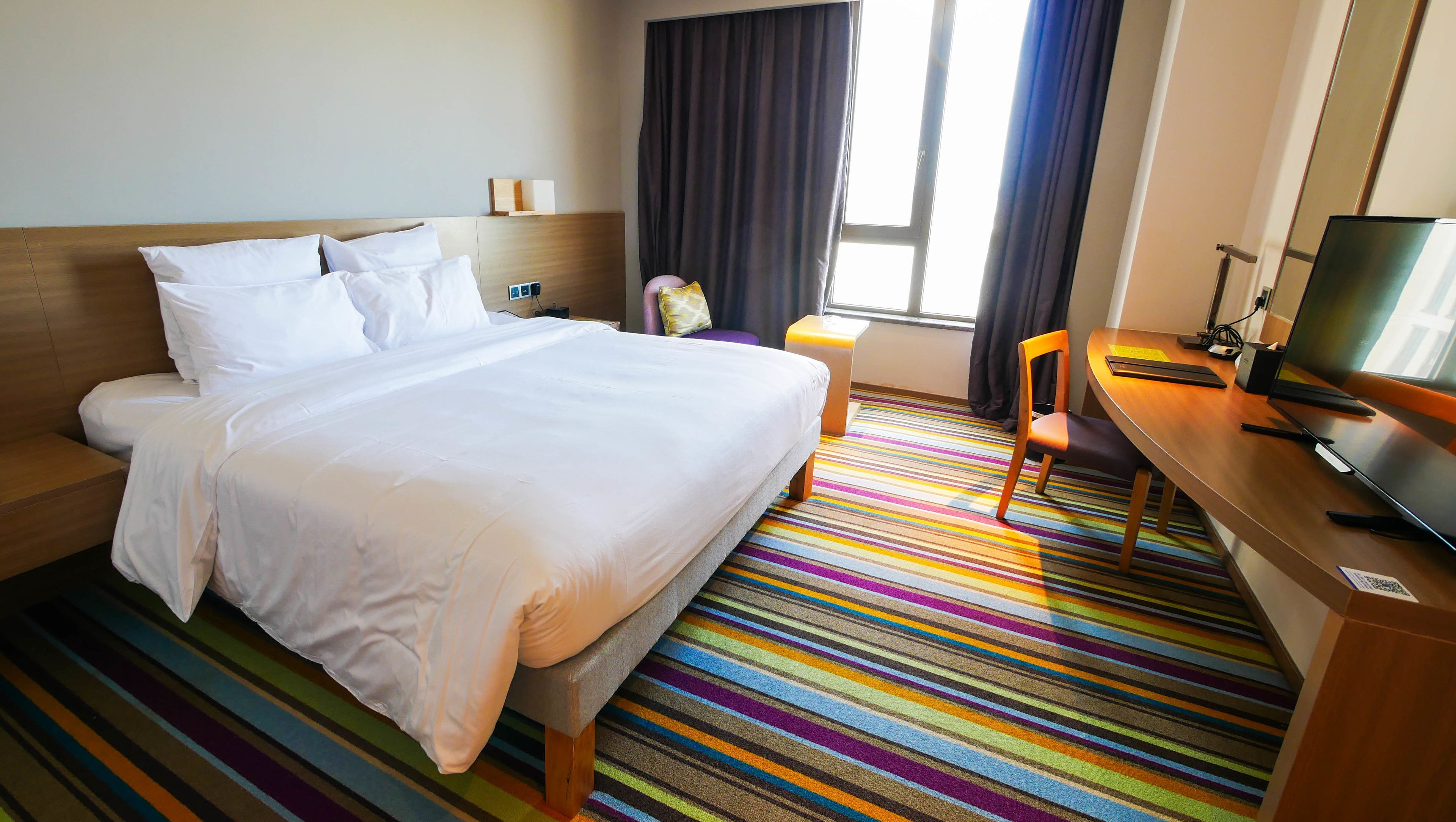 A hotel room with a bed, a desk, a chair, a television, and a window with curtains.