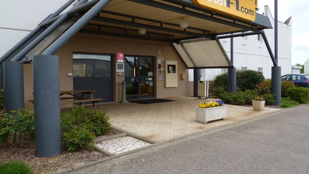 Entrada de hotel con un área de estar al aire libre techada, una puerta de acceso visible y un cartel.
