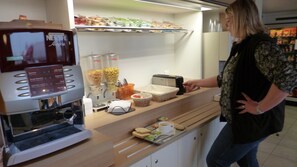 Una estación de café con una máquina de café, un tostador y diversos alimentos sobre una encimera.