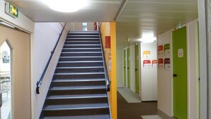 Pasillo de hotel de varios niveles con una escalera, puertas verdes y blancas, y señales de salida de emergencia.