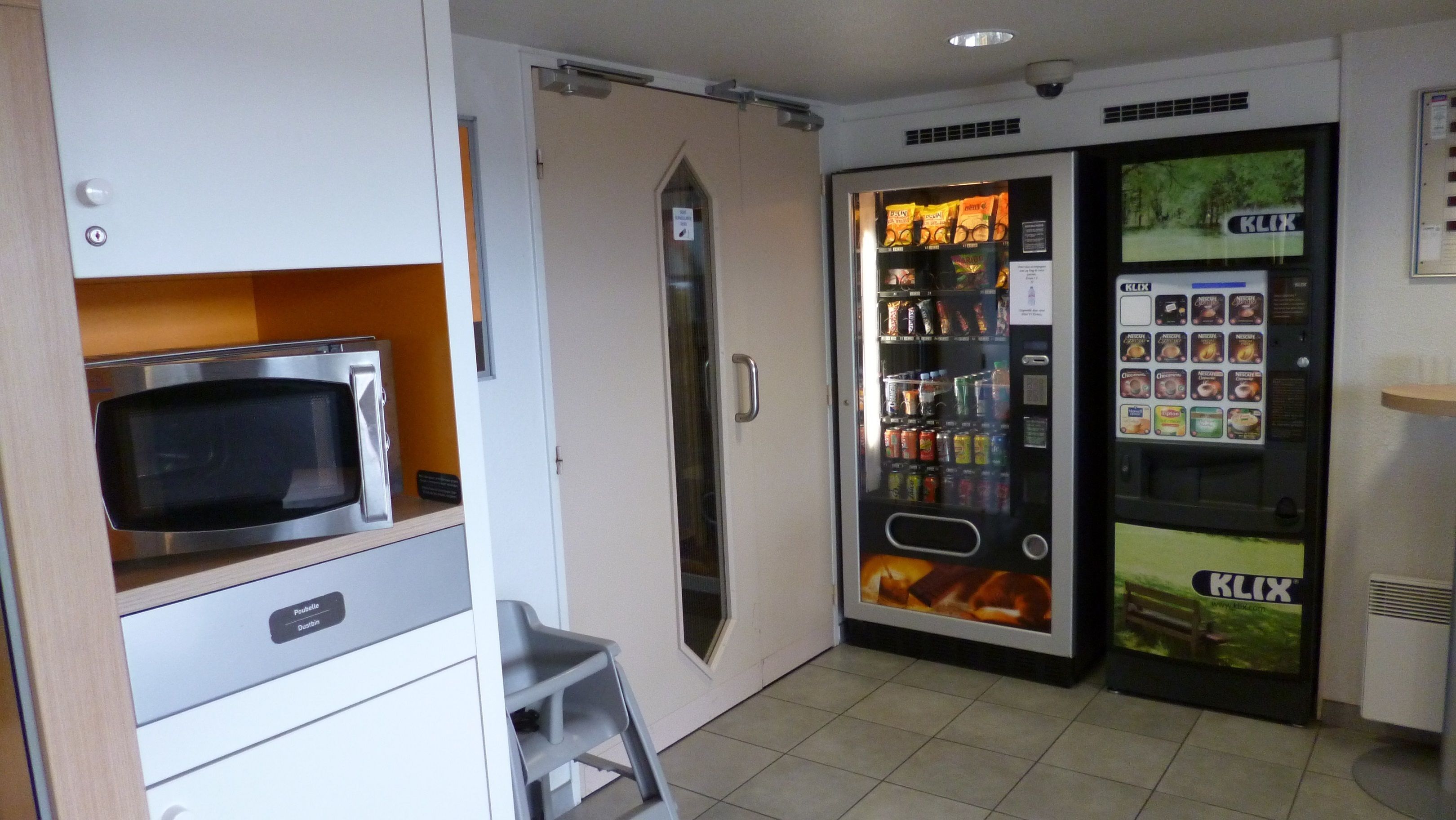 Una kitchenette con microondas, refrigerador y máquina expendedora de bebidas.