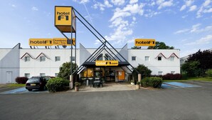 Un hotel de diseño moderno, con un llamativo letrero 'hotel F1', una dirección web y una zona de estacionamiento.