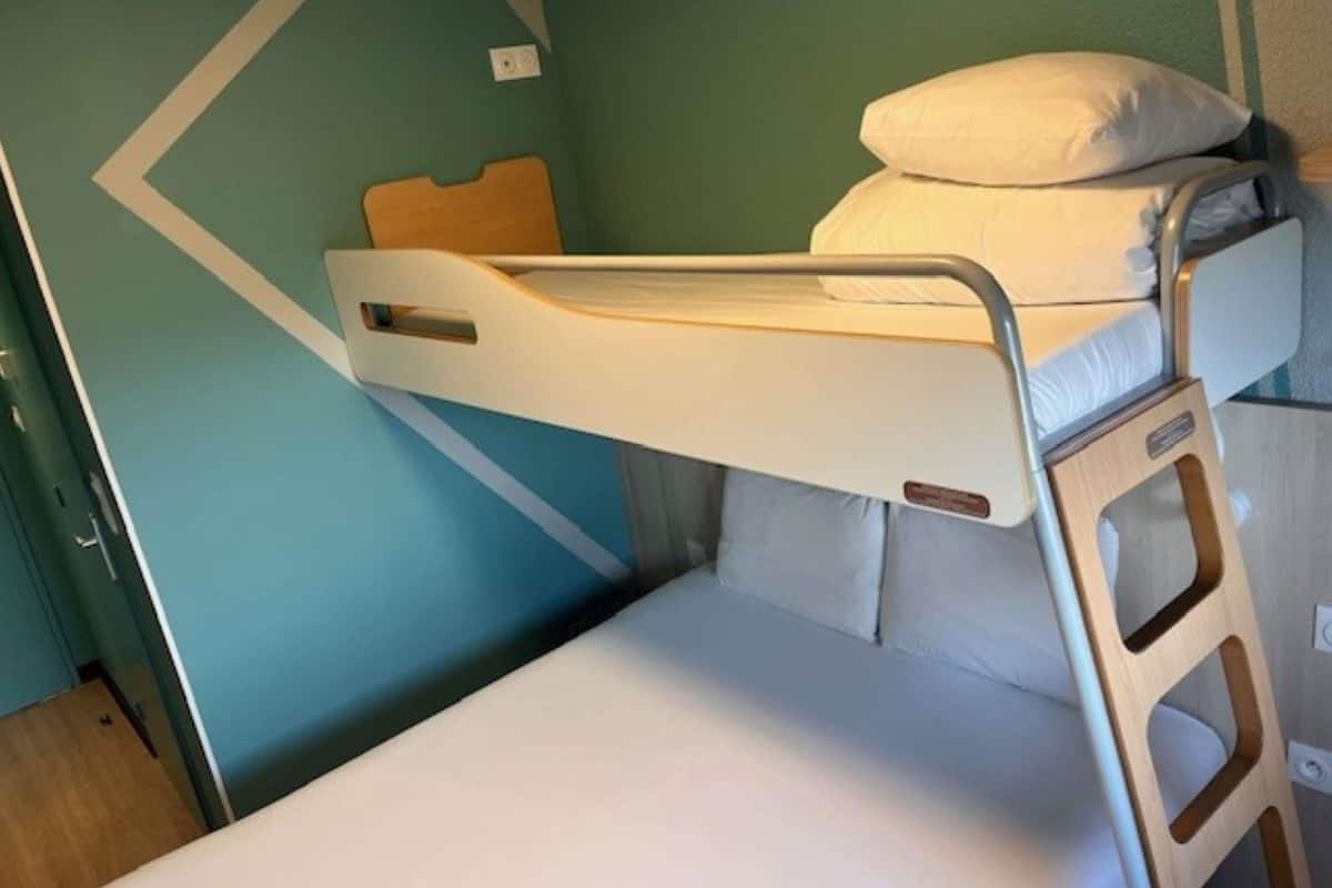 Un lit superposé avec une tête de lit, un oreiller et une échelle en bois.
