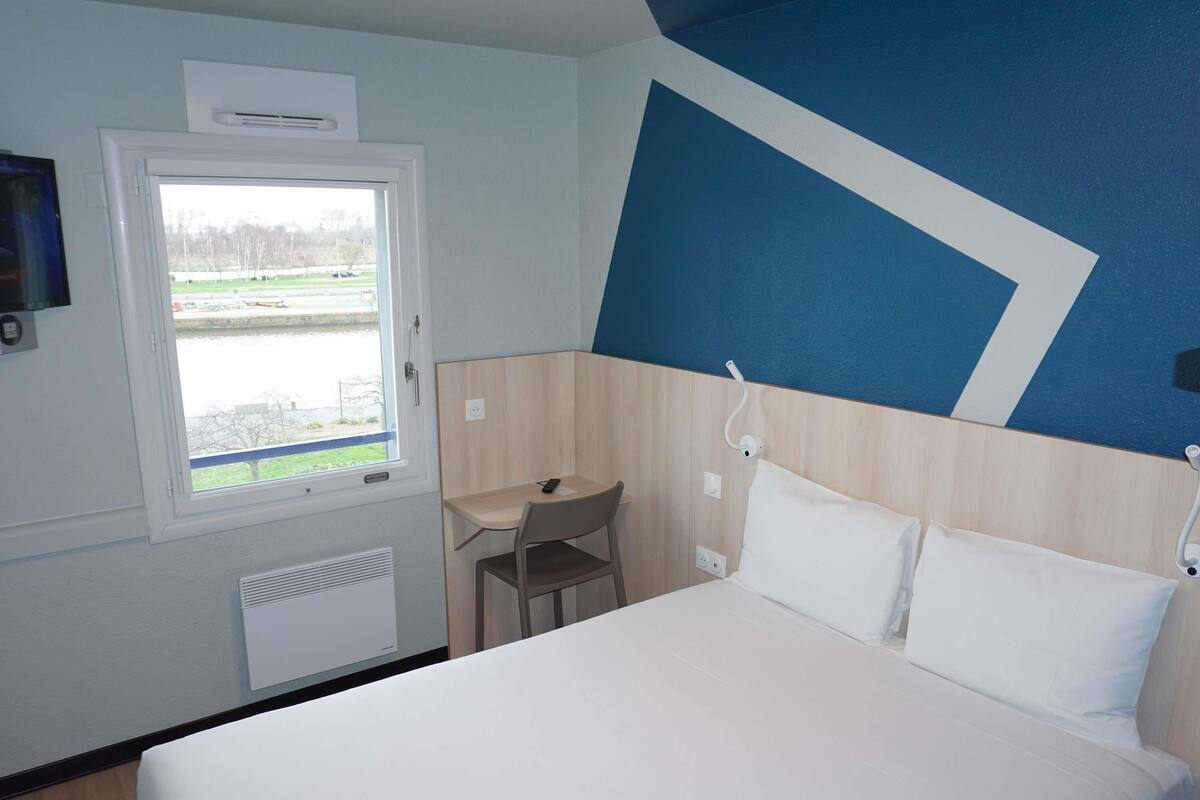 A hotel room with a bed, a desk, and a window.