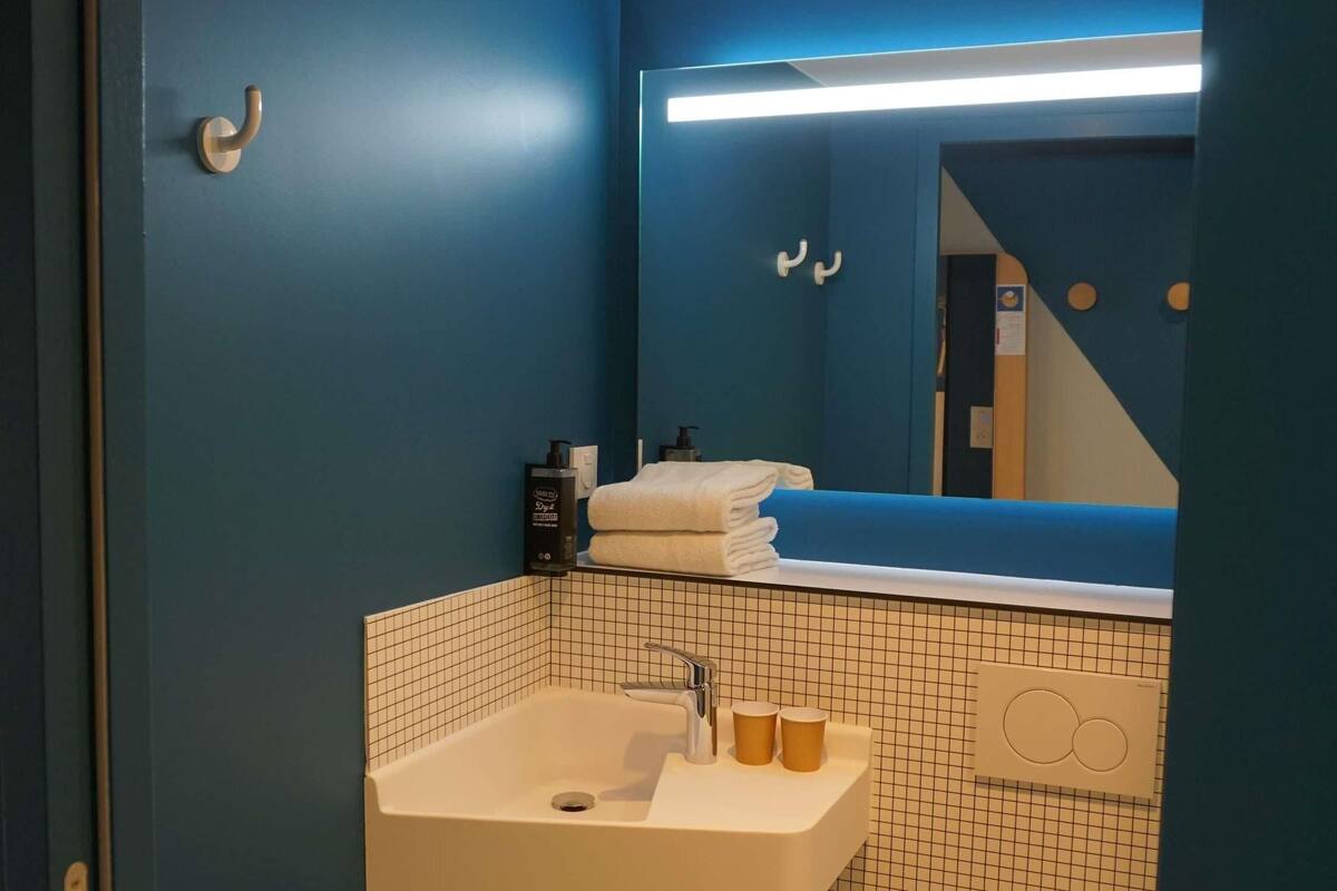 Une salle de bain avec un lavabo blanc, un miroir, des toilettes et un mur bleu.