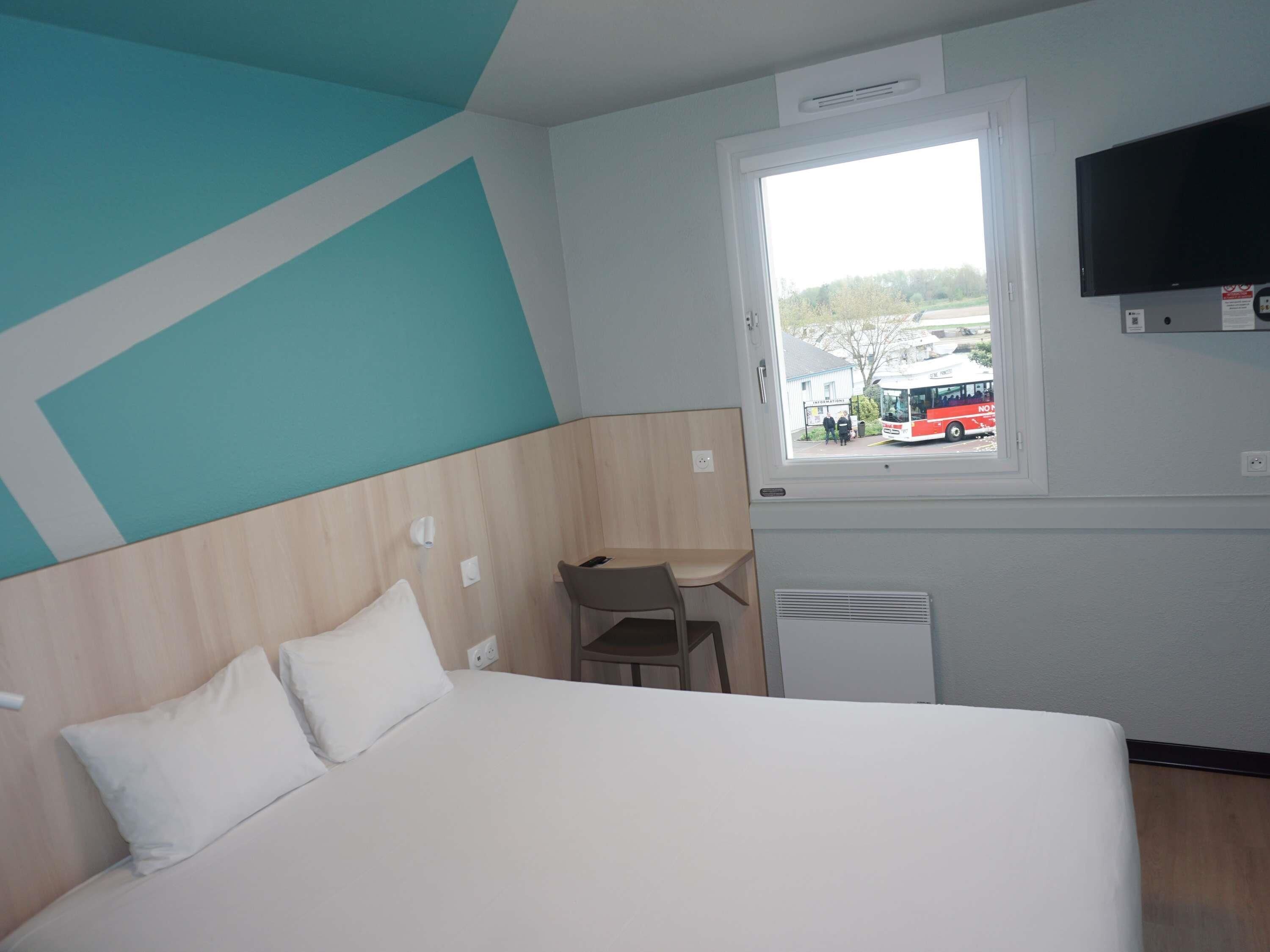 A hotel room with a bed, a desk, a chair, a TV, and a window with a view of the outside.