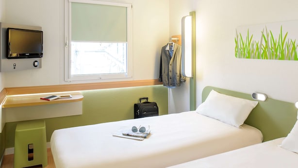 Habitación de hotel con cama, escritorio con silla, televisor y ventana con vista a edificios.