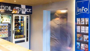 Una máquina expendedora con aperitivos y bebidas, un cartel de servicios e un mostrador de información con folletos.