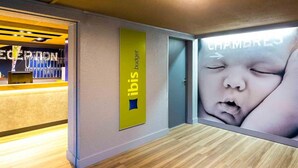 Una zona de recepción con un letrero de 'ibis budget', suelo de madera y una puerta de vidrio que da a una habitación.