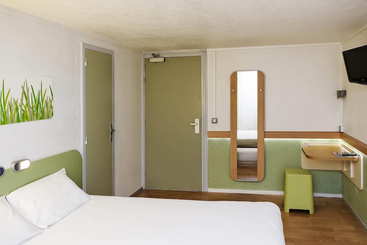 Een hotelkamer met een bed, een deur, een spiegel, een wastafel en een televisie.