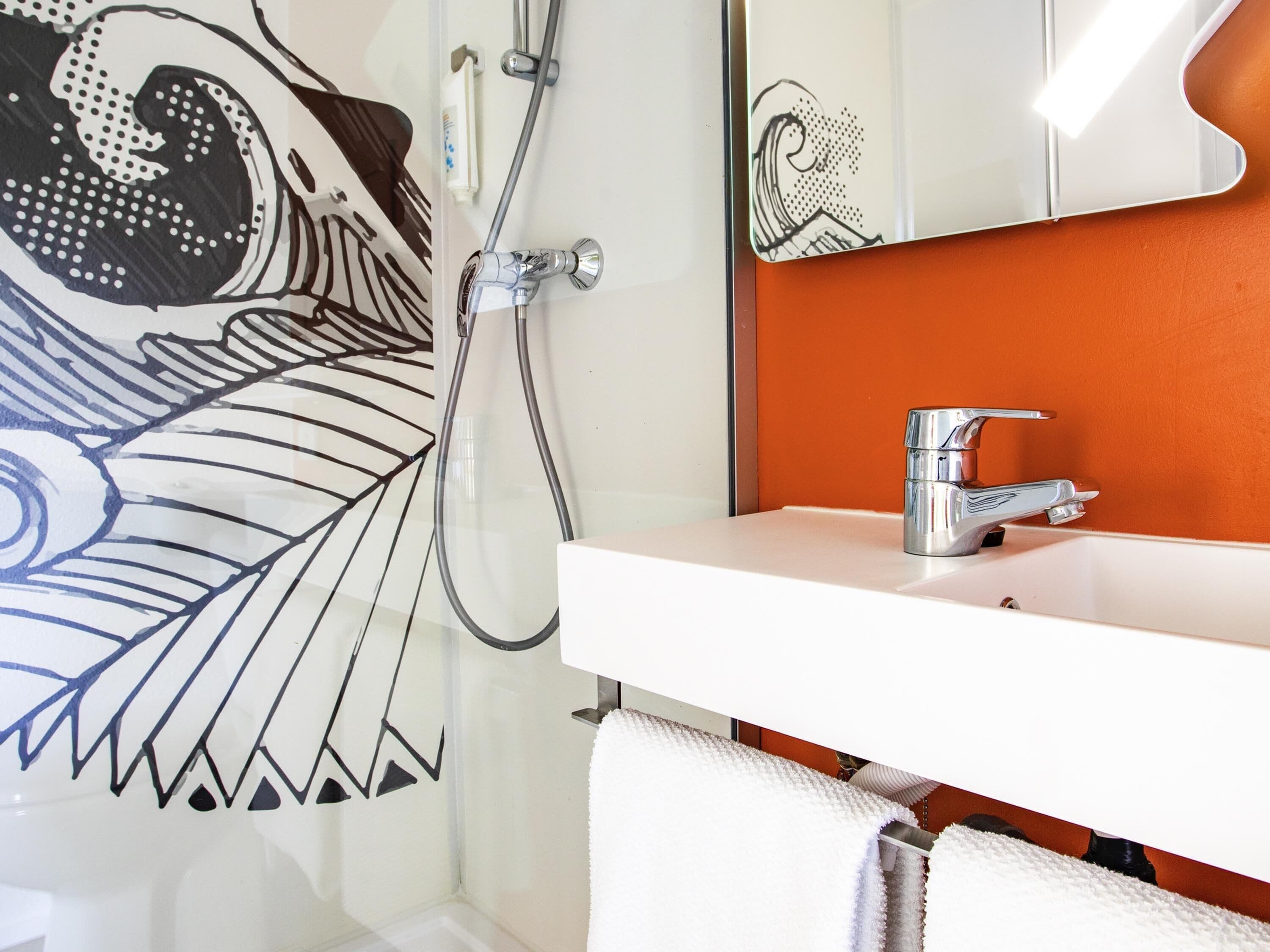 A bathroom with a white sink, a mirror, and a shower with a hose.