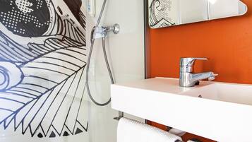A bathroom with a white sink, a mirror, and a shower with a hose.