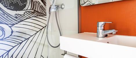 A bathroom with a white sink, a mirror, and a shower with a hose.