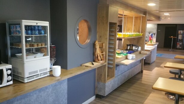 A modern cafe interior with a counter, a refrigerator, and a display case. - ibis budget Flers Les Grands Champs (Flers)