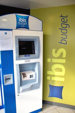 Un quiosco de autoservicio del hotel ibis budget con pantalla digital, ranura para tarjeta y una pequeña pantalla.