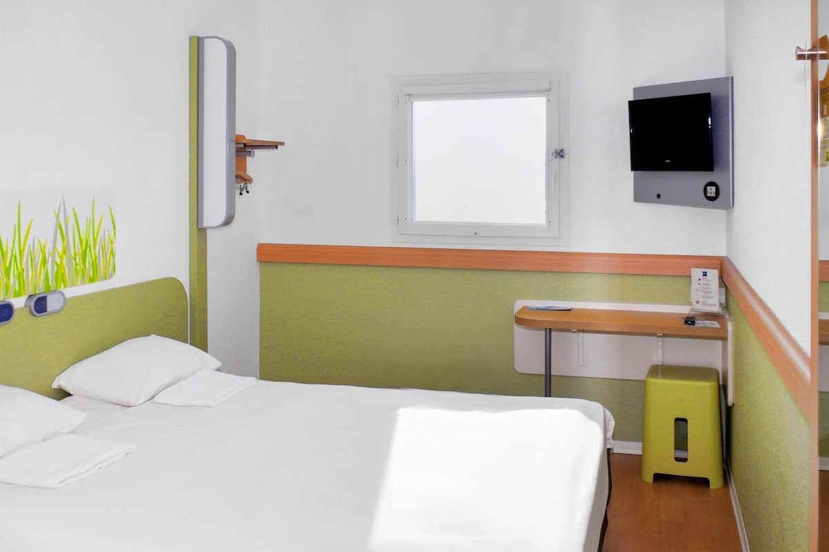 Una habitación de hotel con cama, escritorio, televisor y ventana.