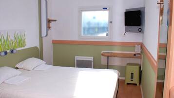 Habitación de hotel con cama, televisión, ventana y escritorio pequeño.
