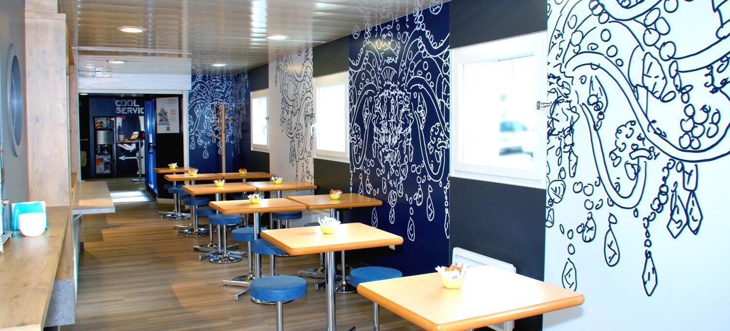 A modern cafe with wooden tables and blue chairs, featuring a wall with intricate black line drawings.