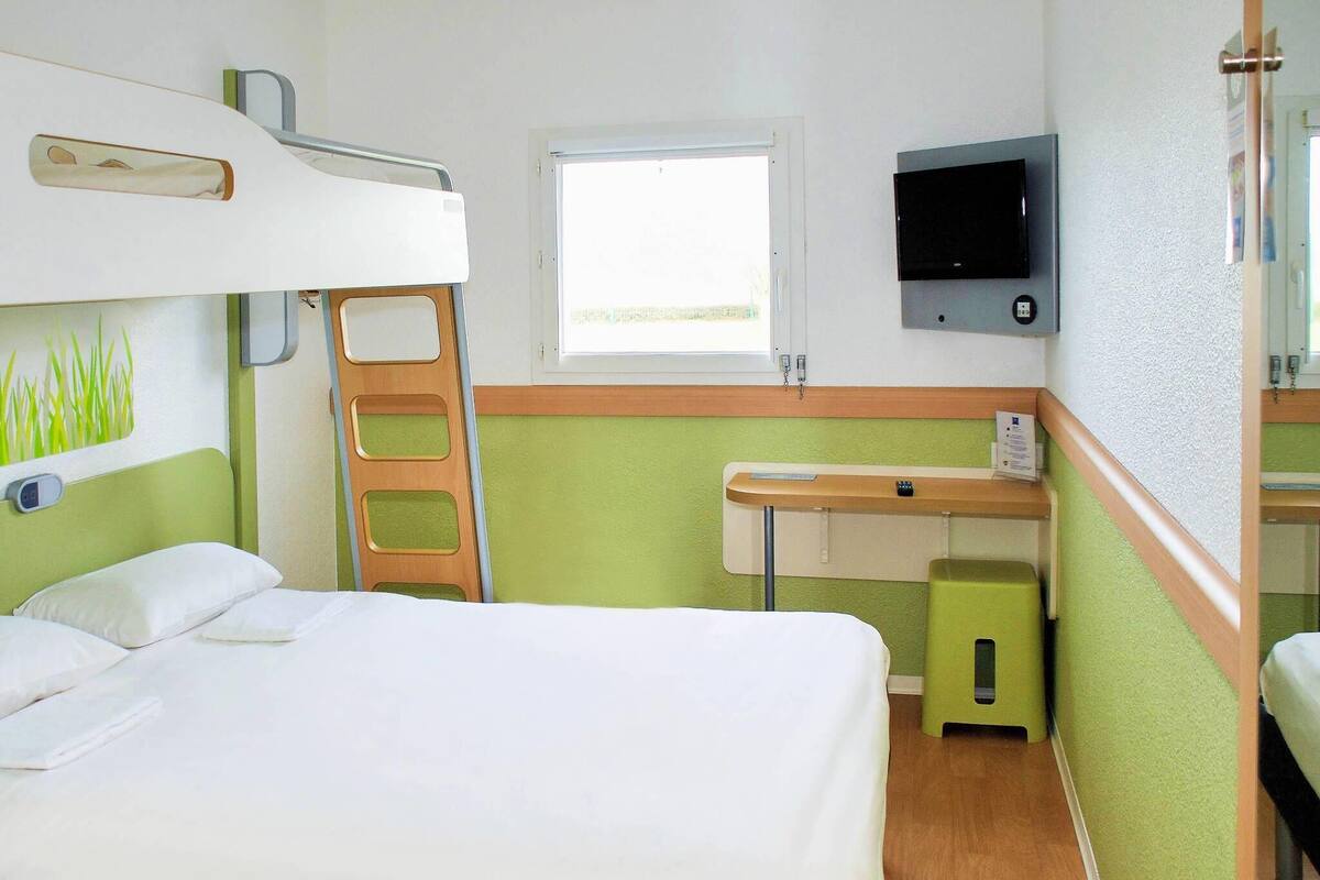 Una habitación de hotel con una cama litera, un escritorio con silla, un televisor y una ventana.