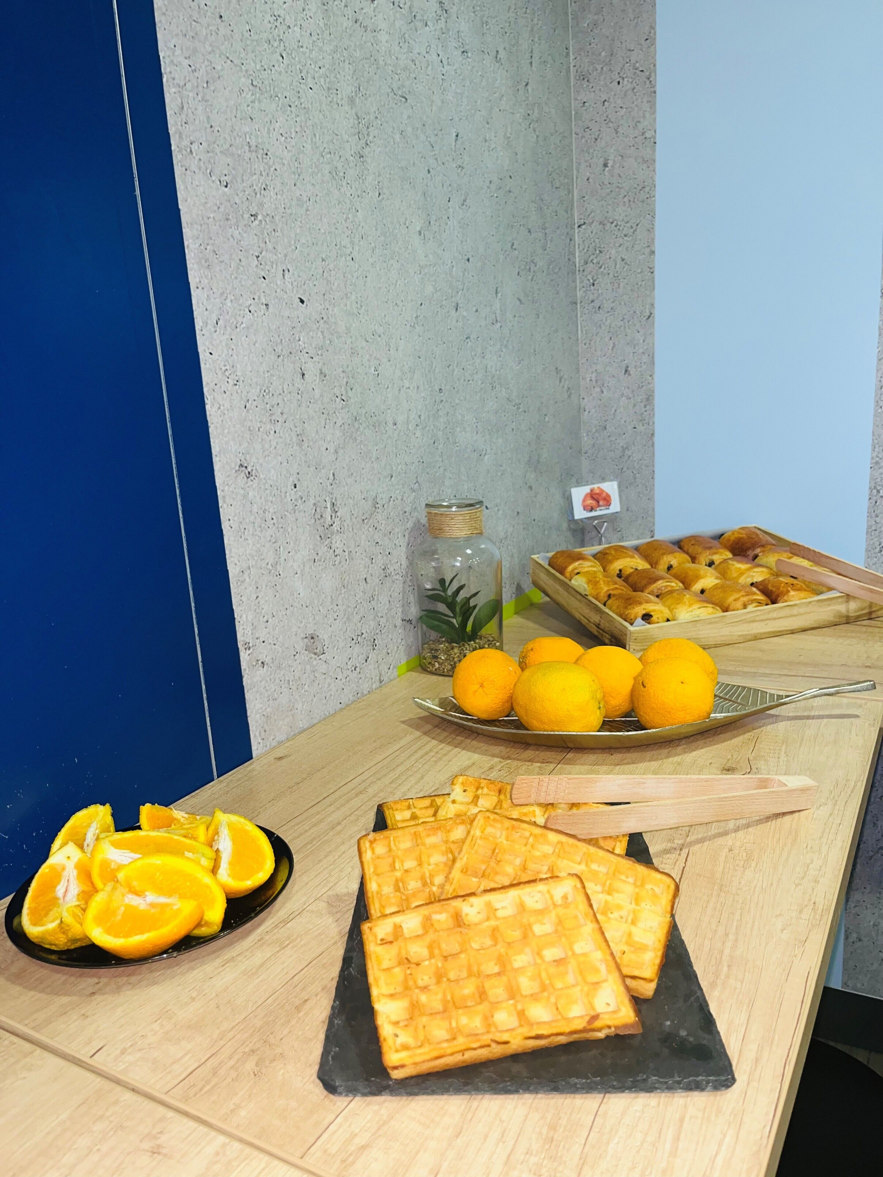A breakfast table with waffles, sliced oranges, and a tray of croissants.