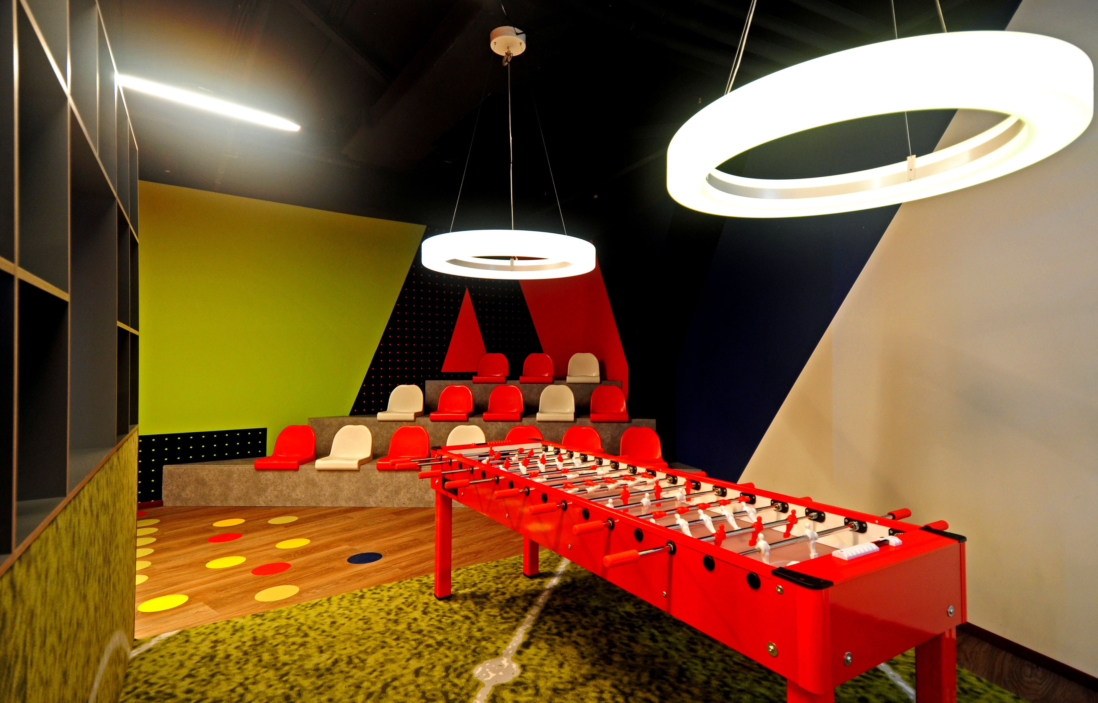 Una habitación luminosa con una mesa de fútbol de mesa, una zona de juegos colorida y un área de descanso con sillas rojas y beige.