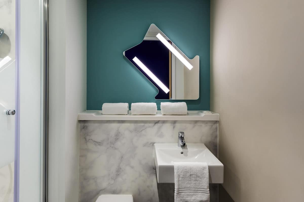 Un baño con un lavamanos blanco, un espejo y una pared color turquesa.