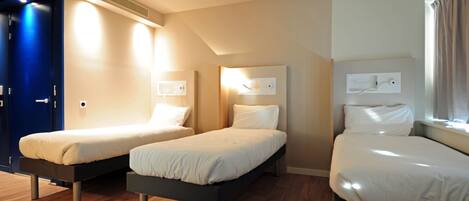 Habitación de hotel con tres camas individuales, suelo de madera y una puerta azul.
