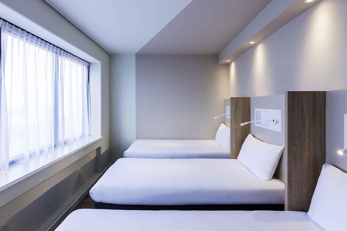 Una habitación de hotel moderna con dos camas individuales, un ventanal con cortinas translúcidas y un diseño minimalista.