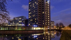 Een modern hotel met een opvallend 'ibis budget'-bord, weerspiegeld in kalm water, omgeven door stadsgebouwen en een heldere lucht.