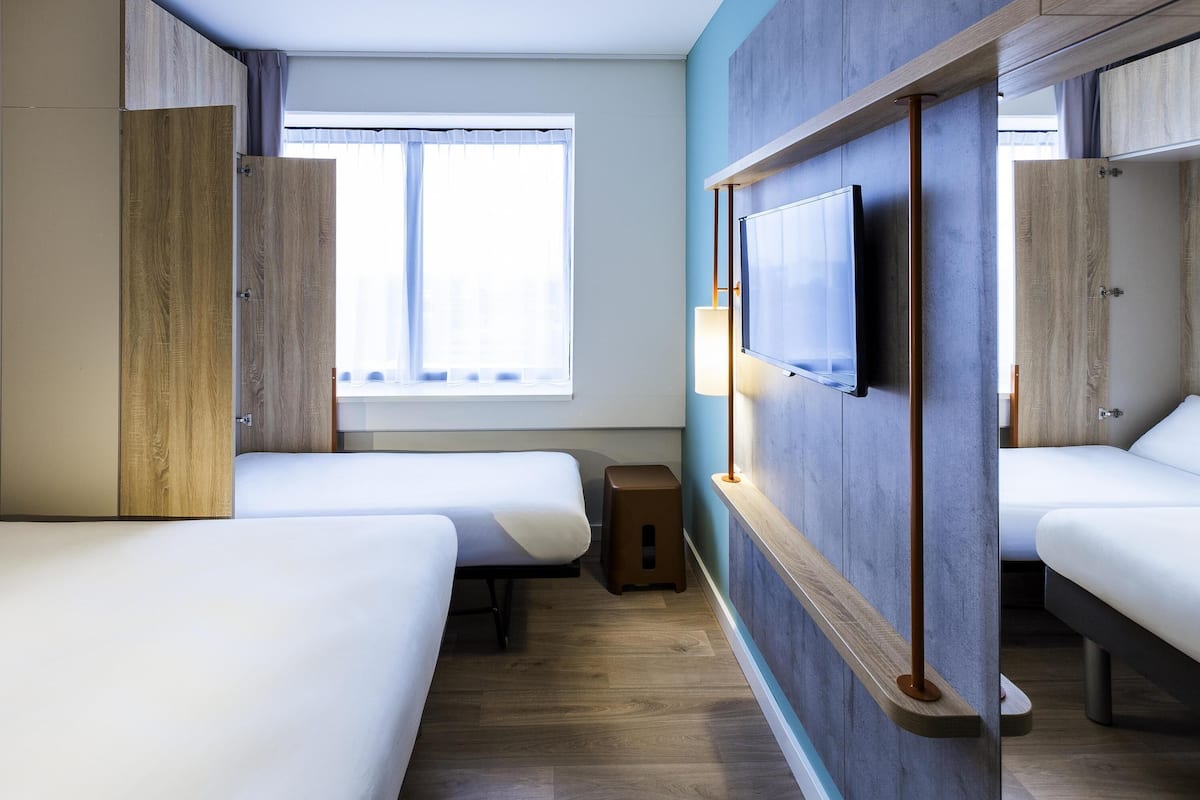 Habitación de hotel con dos camas, televisión y ventana con cortinas.