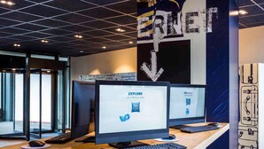 Een werkplek met twee schermen, een toetsenbord, een muis en een smartphone op een houten bureau.